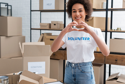 cheerful african american woman showing heart sign while working in charity storehouse