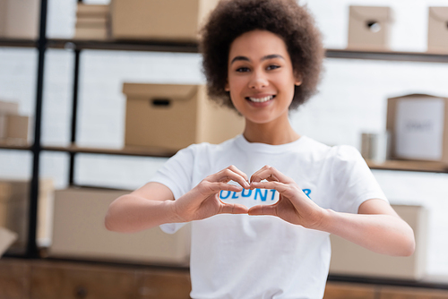 cheerful african american volunteer showing love sign on blurred background