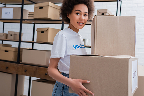 young african american volunteer holding donation boxes and smiling at camera