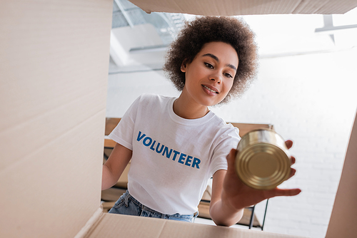 bottom view of smiling african american woman with tin near carton box