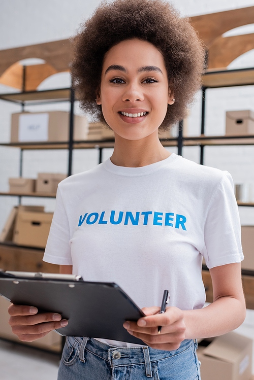 pretty african american volunteer with clipboard smiling at camera on blurred foreground