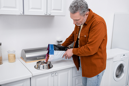 Mature man pouring dog food in bowl in kitchen