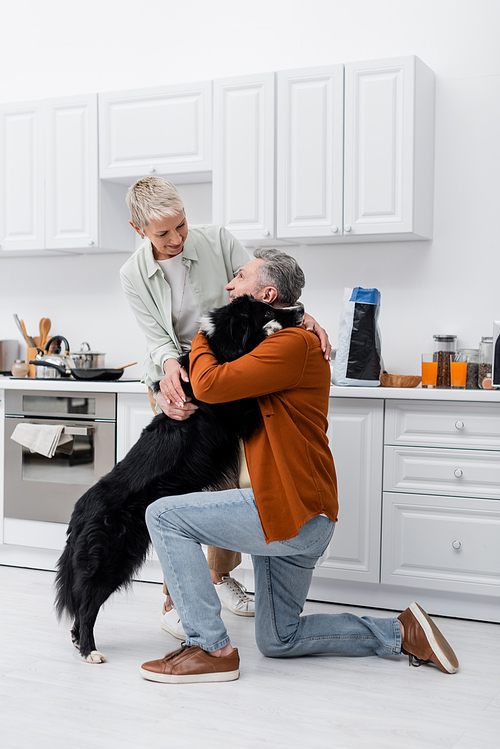 Smiling man hugging border collie near wife in kitchen