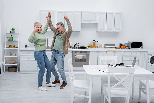 Happy couple dancing near papers and gadgets in kitchen