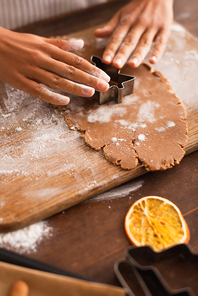 Cropped view of african american woman pressing christmas cookie cutter on dough in kitchen
