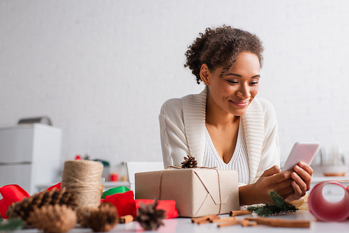 African american woman using smartphone near present and blurred decor at home