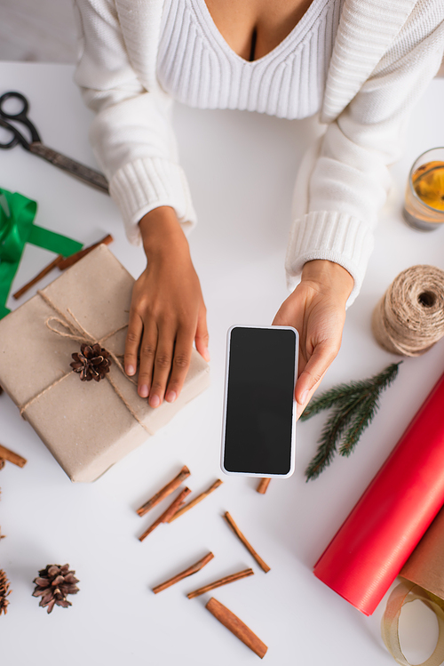 Top view of african american woman holding smartphone near present and christmas decor at home