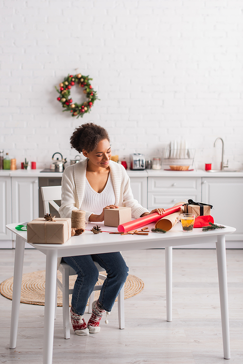 Smiling african american woman looking at gift box and christmas decor at home