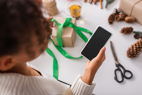 Overhead view of african american woman holding cellphone near blurred christmas gifts