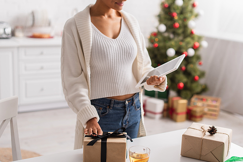 Cropped view of african american woman holding digital tablet near tea and christmas gifts