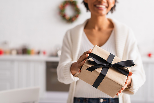 Cropped view of christmas gift in hands of blurred african american woman at home