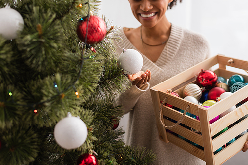 Cropped view of christmas tree near blurred african american woman with baubles at home