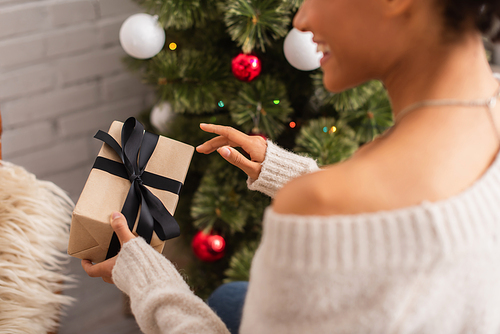 Cropped view of gift box in hands of blurred african american woman near christmas tree