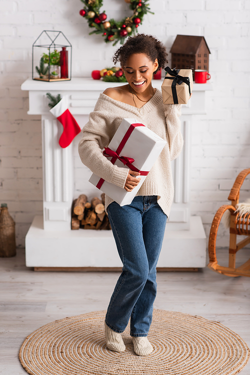 Cheerful african american woman holding presents near fireplace and christmas wreath