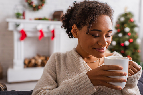 Smiling african american woman holding cup during christmas at home