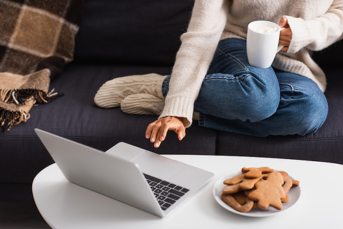 Cropped view of african american woman with cup using laptop near christmas gingerbreads