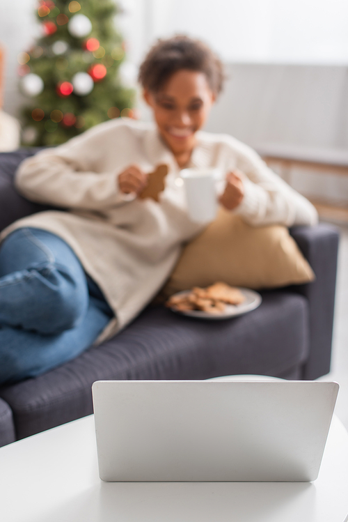 Laptop near blurred african american woman and christmas tree at home