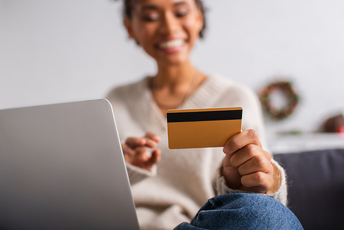Credit card in hand of blurred african american woman near laptop at home