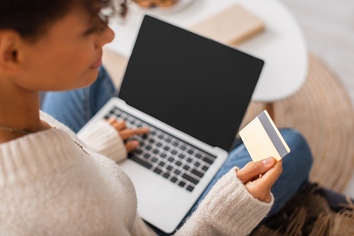 Blurred african american woman holding credit card and laptop at home