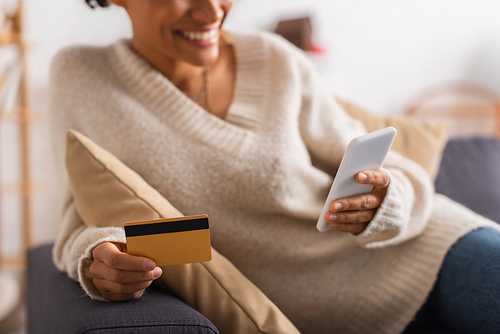 Cropped view of smiling african american woman using cellphone and credit card at home