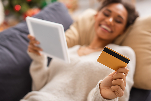 Blurred african american woman holding digital tablet and credit card at home