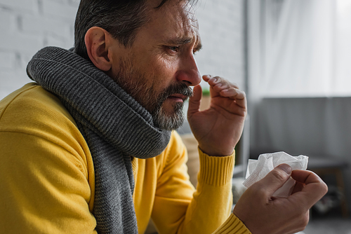 sick man with sore throat and runny nose wearing warm scarf and holding paper napkin