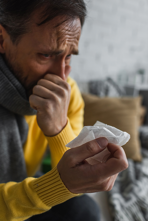 sick man in warm scarf holding paper napkin and sneezing at home