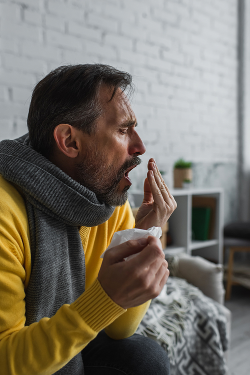 ill man with pneumonia sitting in warm scarf and couching at home