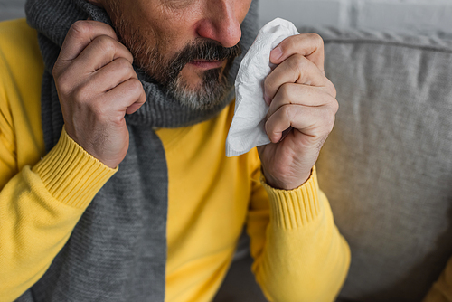 partial view of ill man in warm scarf holding paper napkin