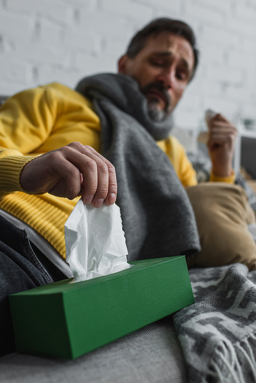 sick man in warm scarf taking paper napkin from pack on blurred background