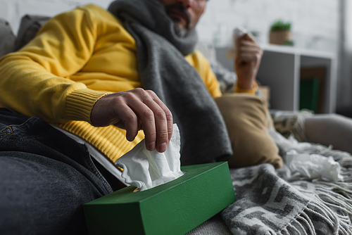 partial view of ill man lying on couch and taking paper napkin from pack