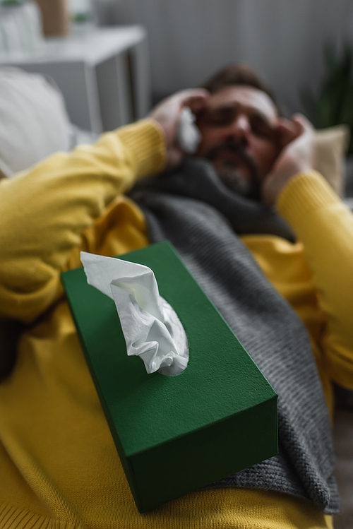 selective focus of pack with paper napkins near sick man lying and suffering from headache on blurred background