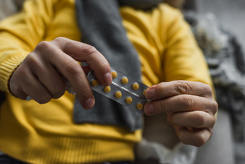 selective focus of pills in hands of cropped sick man lying on blurred background