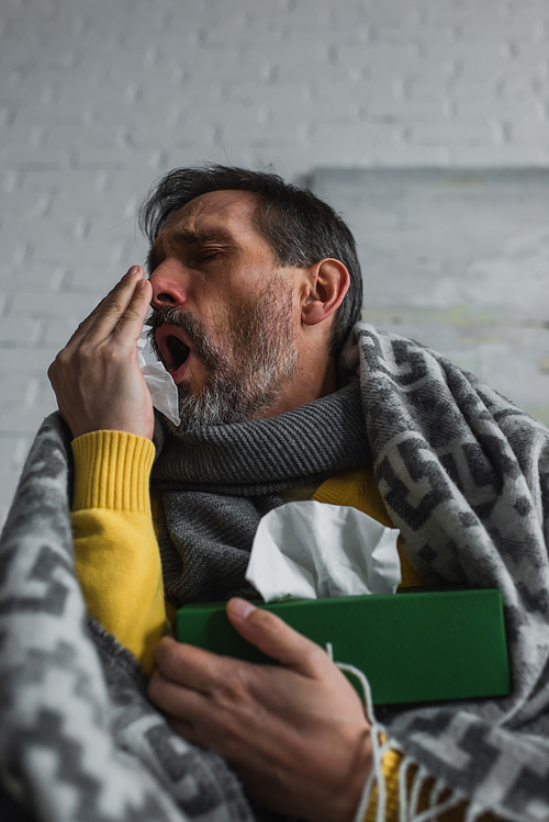 low angle view of man covering mouth with hand while coughing and holding pack of paper napkins