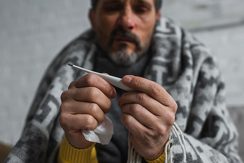 selective focus of electronic thermometer in hands of ill man on blurred background