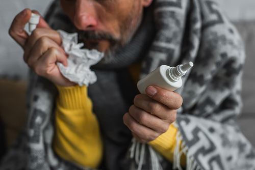 partial view of blurred man holding nasal spray and crumpled paper napkin while suffering from runny nose