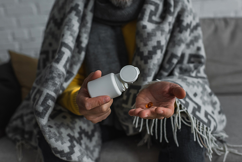 cropped view of diseased man under warm blanket holding container and pill