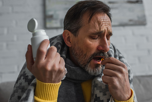 diseased man with closed eyes holding container and taking pill at home