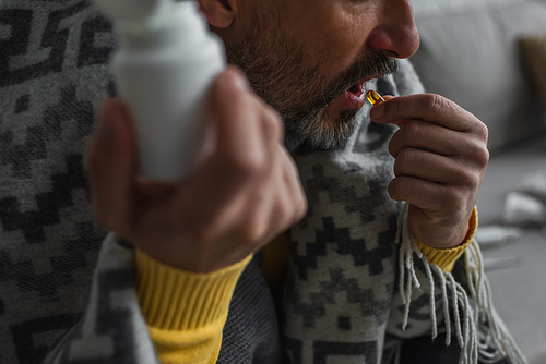 cropped view of sick man taking pill while holding container on blurred foreground