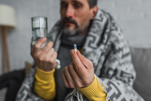 sick man holding pill and glass of water on blurred background