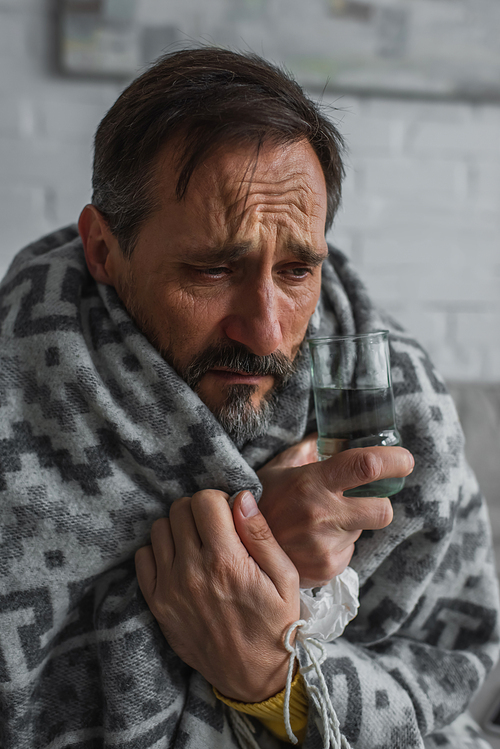 diseased man wrapped in warm blanket holding glass of water