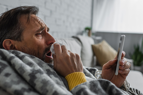 sick man with paper napkin coughing while looking at mobile phone