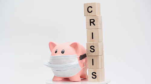 piggy bank in medical mask and blocks with crisis word on white surface