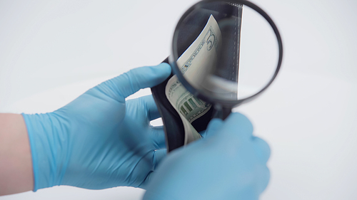 cropped view of person holding magnifying glass near wallet with dollar banknote on white background