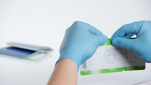 cropped view of man in latex gloves tearing boarding pass near blurred passport on white background