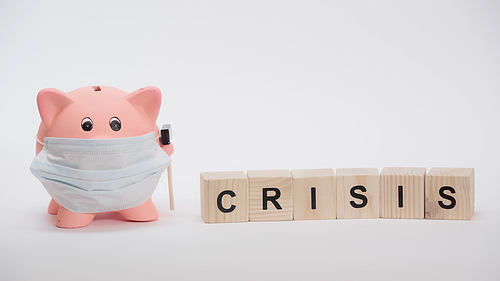 piggy bank in protective medical mask and cubes with crisis word on white surface