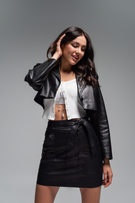 cheerful young woman in leather autumnal outfit smiling isolated on grey