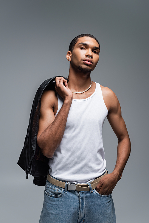 muscular young african american man in tank top holding leather jacket isolated on grey