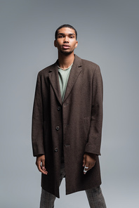 young african american man in woolen coat looking at camera isolated on grey