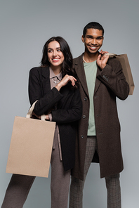 happy interracial couple in stylish outfits holding shopping bags isolated on grey